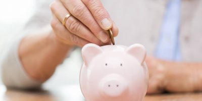 senior-woman-hand-putting-money-to-piggy-bank